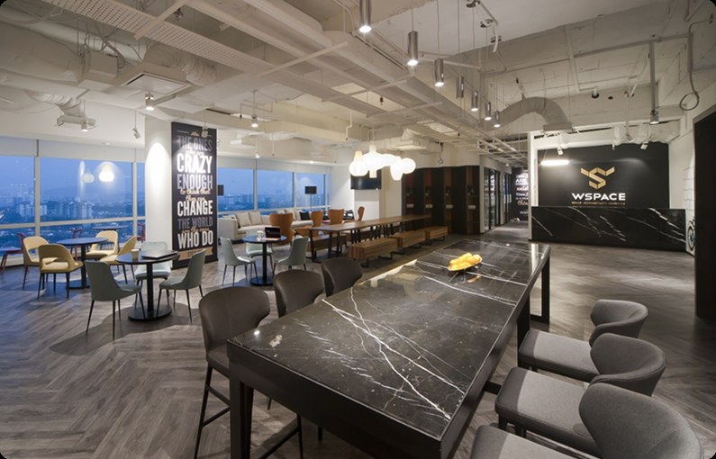 Interior of a WSPACE coworking space in Kuala Lumpur, showing lounge seating, a marble bar table and the WSPACE logo on the reception wall